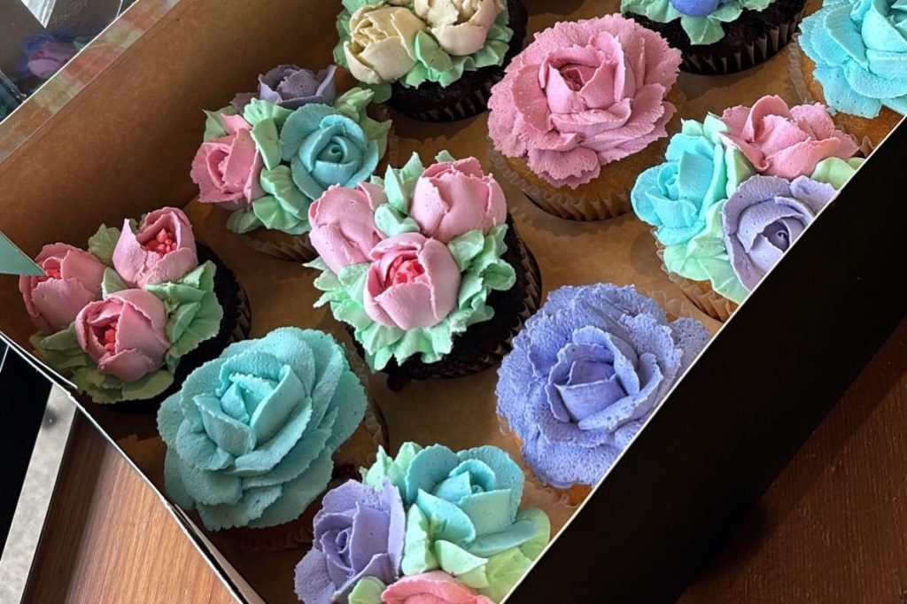 Box of cupcakes piped with buttercream tulips, roses and leaves in pink, blue and purple